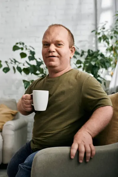 A man with inclusivity sits casually on a couch in a home setting, holding a white mug, enjoying a moment of relaxation. — Stock Photo