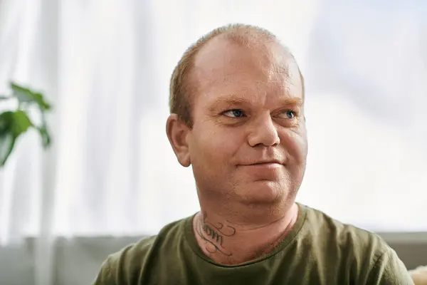 A man with inclusivity in casual attire sits at home, looking thoughtfully off-camera. — Stock Photo