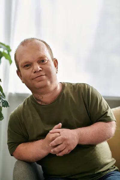 A man with inclusivity in casual attire sits comfortably on a couch in his home. — Stock Photo
