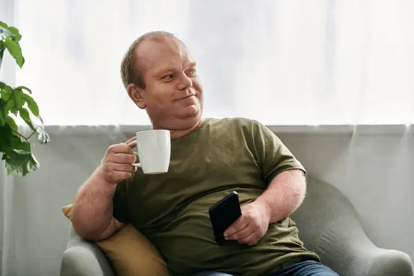 A man with inclusivity sits comfortably in a chair at home, enjoying a cup of coffee. — Stock Photo