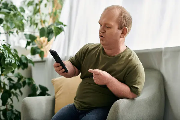 Ein Mann mit Inklusivität sitzt zu Hause in einem Stuhl, lässig gekleidet, und schaut auf sein Handy. — Stockfoto