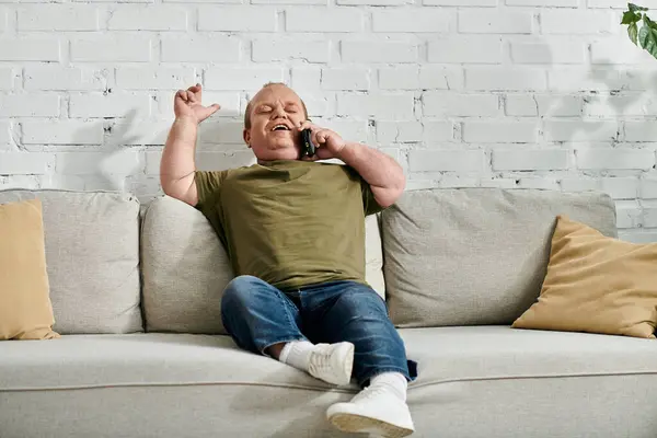 Un homme inclusif assis sur un canapé, souriant et parlant au téléphone. — Photo de stock