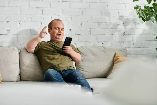 A man with inclusivity sits on a couch, relaxed and comfortable in casual attire. — Stock Photo