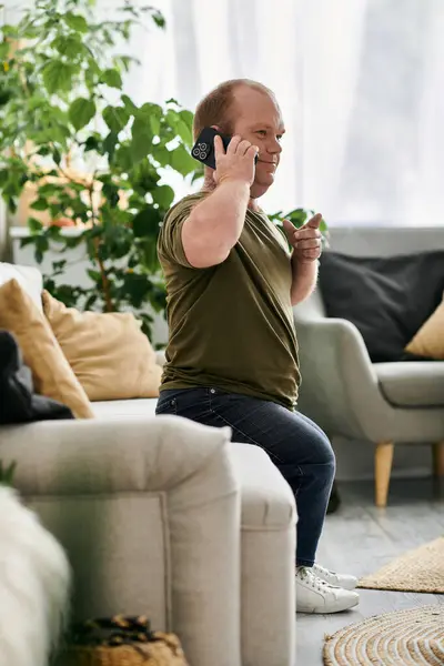 A man with inclusivity sits on a couch in his home, talking on the phone and smiling. — Stock Photo