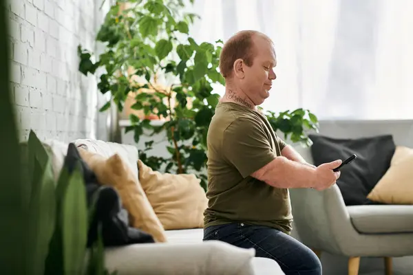 A man with inclusivity sits on a couch in a cozy living room, casually dressed and using his phone. — Stock Photo