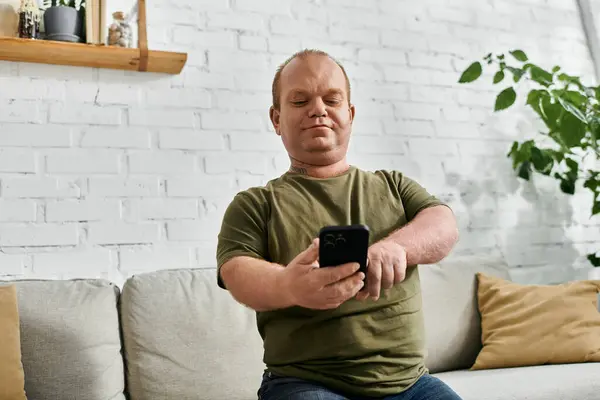 A man with inclusivity in casual attire sits on a couch in a living room, looking at his phone. — Stock Photo