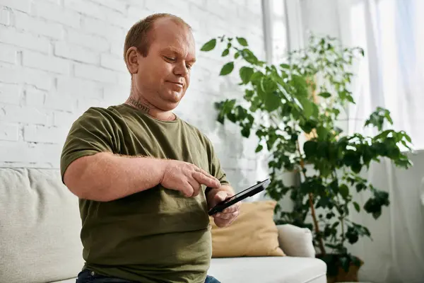 A man with inclusivity sits on a couch in his home, casually dressed and browsing on a tablet. — Stock Photo