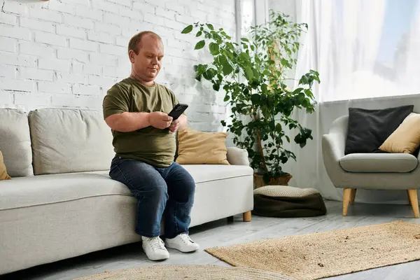 A man with inclusivity sits on a couch in a casual setting, using his phone. — Stock Photo