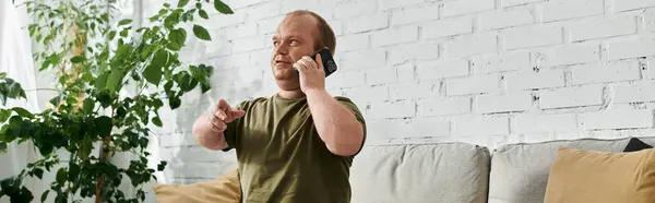 A man with inclusivity sits on a couch in his home, casually dressed and speaking on the phone. — Stockfoto