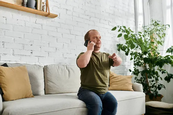 A man with inclusivity sits on a couch, talking on his phone. — Stock Photo