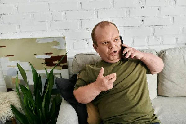 Um homem com inclusividade senta-se em um sofá em casa, vestido casualmente com uma camisa verde, falando ao telefone. — Fotografia de Stock