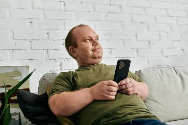 Человек с инклюзивностью расслабляется на диване в своем доме, держа в руках смартфон. — стоковое фото