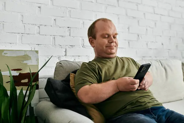 A man with inclusivity relaxes on a couch, casually scrolling through his phone. — Stock Photo