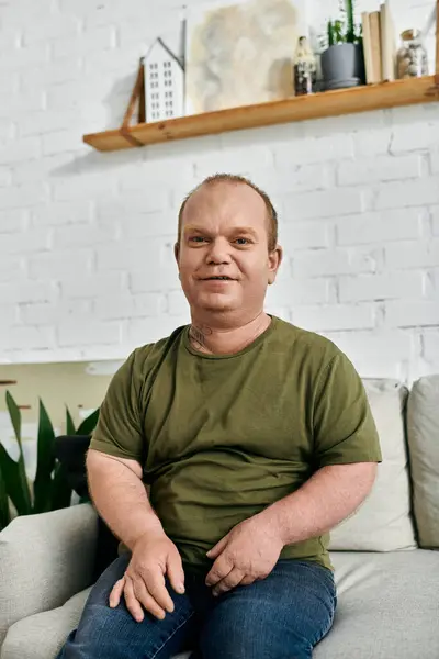A man with inclusivity sits on a couch in his home, wearing casual clothing and smiling at the camera. — Stock Photo