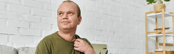 A man with inclusivity relaxes in his home, adjusting his shirt, in casual attire. — Stock Photo
