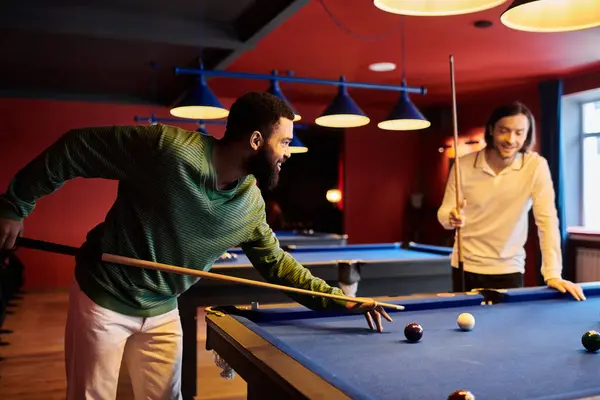 Friends play a casual game of billiards in a dimly lit lounge. — Stock Photo