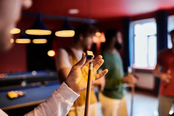 A man holds a cue stick and chalk while playing billiards with friends. — Stock Photo