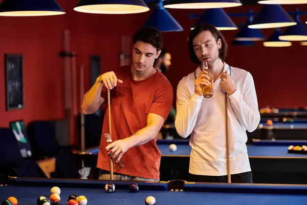 Amici vestiti con disinvoltura, giocare a biliardo e gustare una birra in una sala da biliardo poco illuminata. — Foto stock