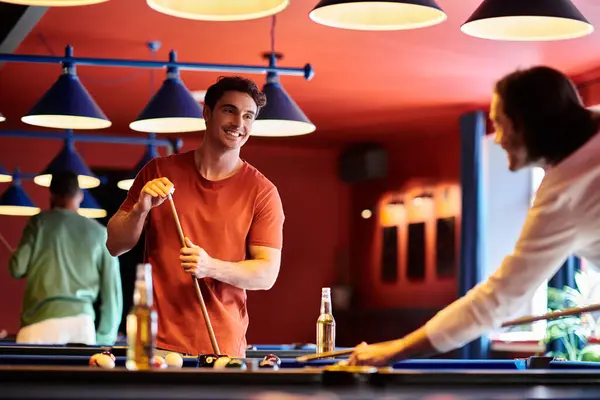 Friends enjoy a casual game of billiards in a bar with a vibrant red wall and blue lights. — Stock Photo