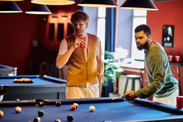 Friends enjoy a casual game of billiards, one taking a shot while the other watches and holds a drink. — Stock Photo