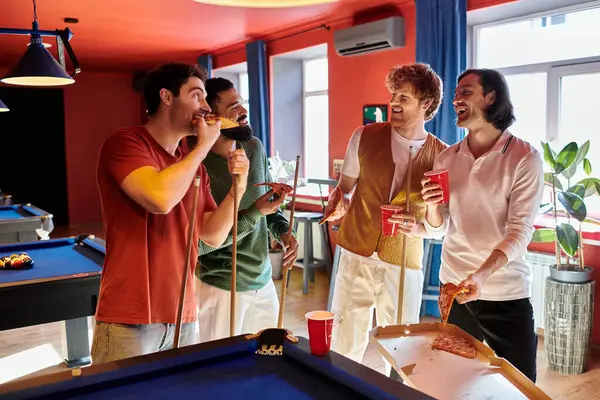 Amigos se reúnem em torno de uma mesa de bilhar, desfrutando de pizza e bebidas enquanto fazem uma pausa de seu jogo. — Fotografia de Stock