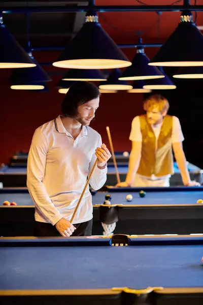 Friends play billiards, one focusing intently on his shot. — Stock Photo