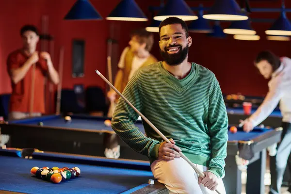 A man smiles while holding his pool cue, enjoying a casual game of billiards with his friends. — Stock Photo