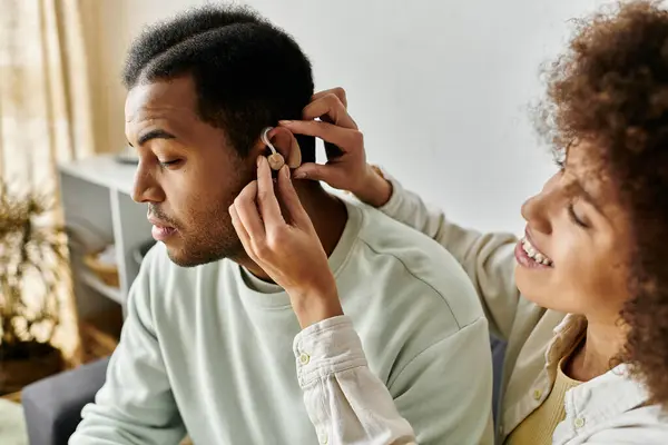 Belle femme afro-américaine aidant son mari avec une aide auditive pendant qu'il est à la maison. — Photo de stock