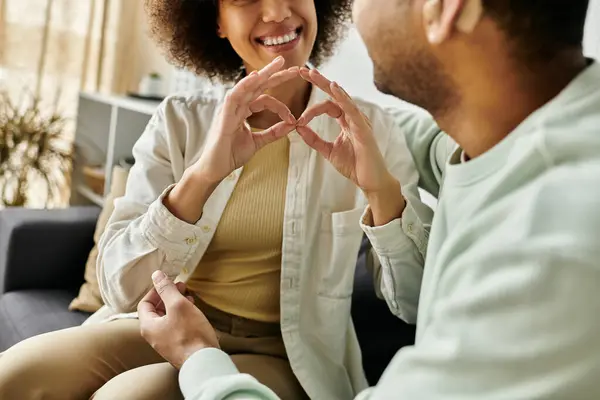 A loving African American couple communicates using sign language while sitting on a couch in their home. — Stock Photo