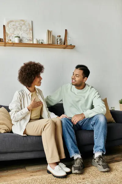 Una pareja afroamericana se sienta en un sofá en casa, comunicándose a través del lenguaje de señas. - foto de stock
