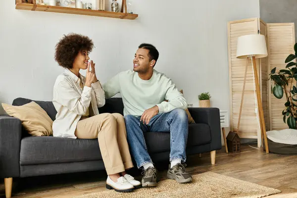 Una bella coppia afroamericana si siede su un divano, usando il linguaggio dei segni per comunicare. — Foto stock