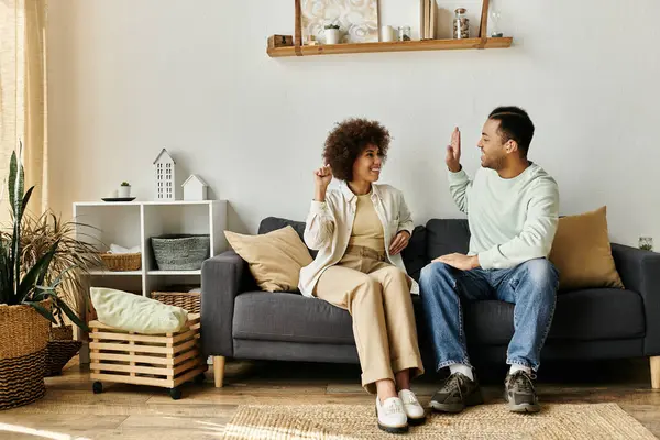 Una pareja afroamericana se sienta en un sofá en su casa, comunicándose con el lenguaje de señas. - foto de stock