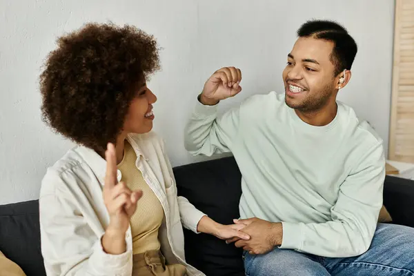 Una bella coppia afroamericana si siede su un divano, usando il linguaggio dei segni per comunicare tra loro. — Foto stock