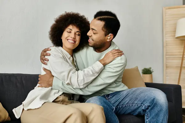 An African American couple sits on a couch, embracing each other. — Stock Photo