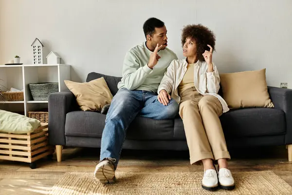 Una pareja afroamericana se sienta en un sofá en su casa, comunicándose a través del lenguaje de señas. - foto de stock