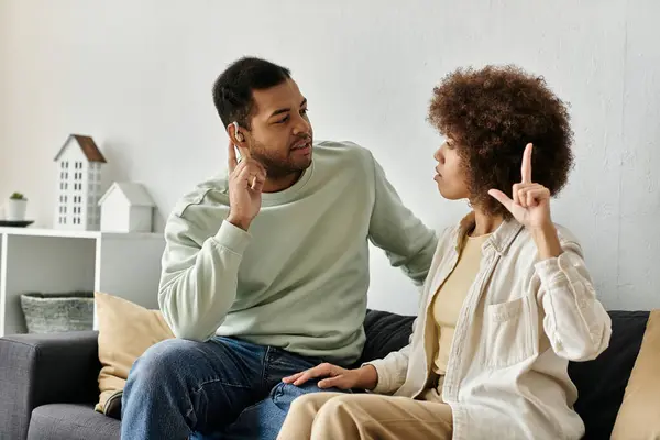 An African American couple uses sign language to communicate while sitting on a couch in their living room. — Stock Photo