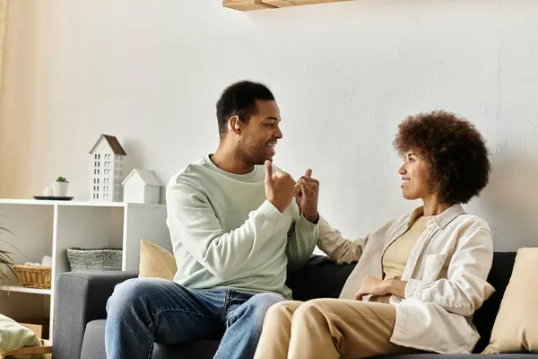 Una coppia afroamericana comunica usando il linguaggio dei segni mentre si rilassa sul divano di casa. — Foto stock