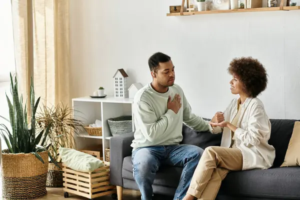 Una pareja afroamericana cariñosa usa el lenguaje de señas para comunicarse mientras está sentada en un sofá en su casa. - foto de stock