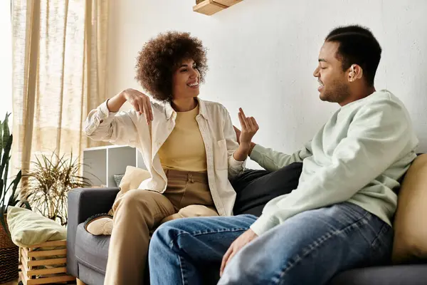 A young African American couple sits on a couch at home, engaging in a lively conversation using sign language. — Stock Photo