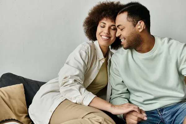 An attractive African American couple sits close together on a couch at home. — Stock Photo