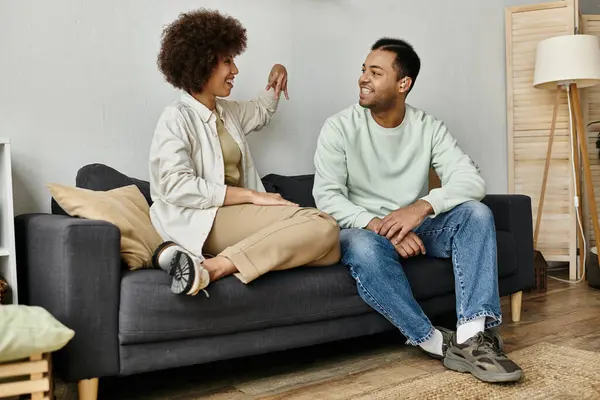 Um casal afro-americano senta-se em um sofá em sua casa, usando linguagem gestual para se comunicar. — Fotografia de Stock
