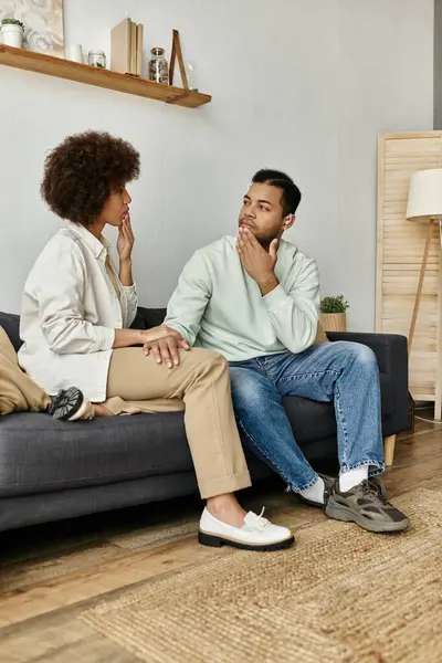Um casal afro-americano amoroso se senta em um sofá, usando linguagem gestual para se comunicar uns com os outros. — Fotografia de Stock