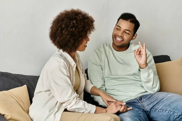 Una pareja afroamericana se sienta en un sofá en casa, usando el lenguaje de señas para comunicarse. — Stock Photo