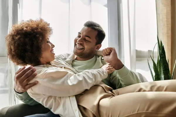 Um casal afro-americano afetuoso, sentado em um sofá enquanto expressa amor genuíno e felicidade. — Fotografia de Stock