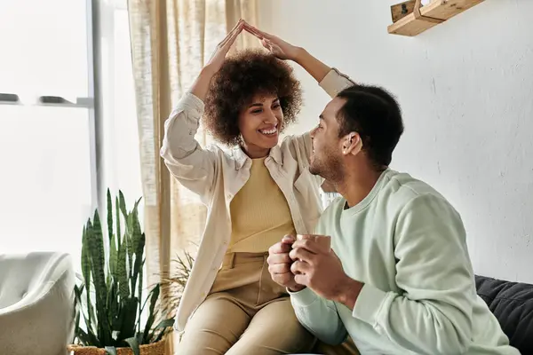 Una pareja afroamericana firma entre sí mientras están sentados en un sofá en su casa. - foto de stock