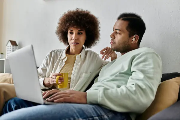 Hermosa mujer afroamericana sentada cerca de su marido con audífono y mirando a la computadora portátil. - foto de stock