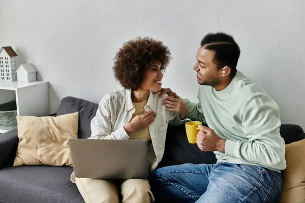 Una atractiva pareja afroamericana utiliza el lenguaje de señas para comunicarse mientras se relaja en un sofá en casa. - foto de stock