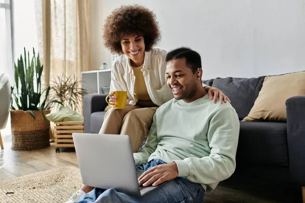 Jovem afro-americana sentada perto de seu marido com aparelho auditivo e olhando para laptop. — Fotografia de Stock