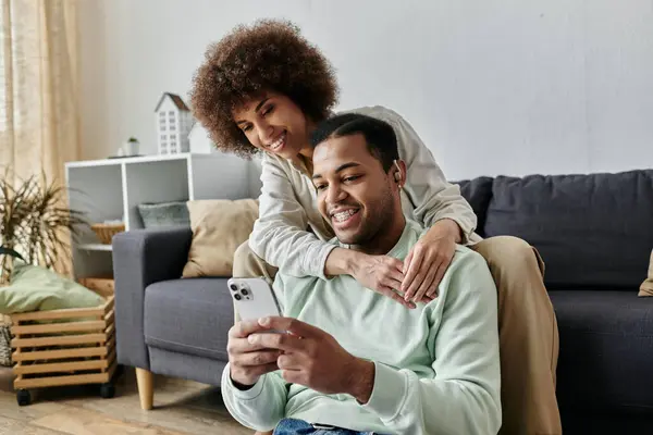 Attractive African American woman sitting near her husband with hearing aid and looking at phone. — Stock Photo