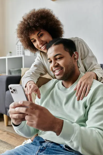 Apelando afro-americano mulher sentado perto de seu marido com aparelho auditivo e olhando para o telefone. — Fotografia de Stock
